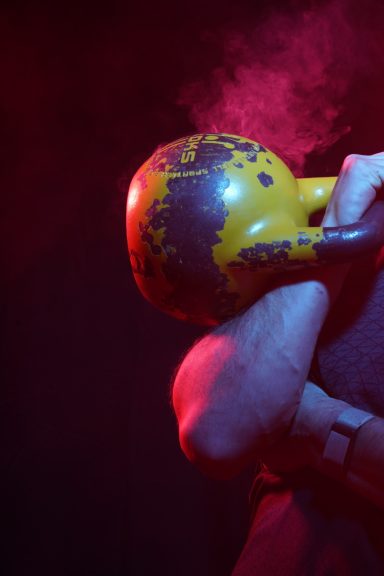 Eine Person hält eine schwere, gelbe Kettlebell vor einem dunklen Hintergrund.
